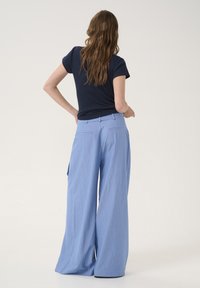 Helleblau gestreifte Stoffhose mit weitem Bein und glatter Textur, ausgestattet mit Gesäßtaschen und Gürtelschlaufen, kombiniert mit einem dunkelblauen T-Shirt.