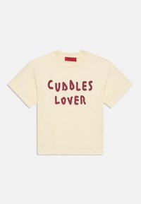Tricou cu mânecă scurtă, culoarea crem, cu gât rotund și text îndrăzneț roșu „CUDDLES LOVER” imprimat pe față.