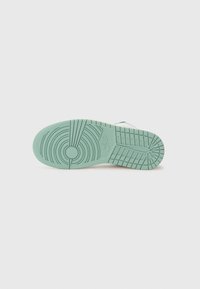 Semelle de basket Nike vert clair avec des motifs circulaires et en grille sur un fond gris clair neutre.