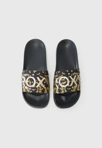 Svarte sandaler med teksturert svart såle. Selen har et gull- og svart organisk mønster med "ROXY" i fet gullskrift.