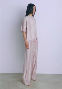 Helles rosa, kurzärmliges Oberteil mit Kragen, kombiniert mit weiten, gestreiften Hosen, die einen verstellbaren Kordelzug mit orangenen Akzenten haben.