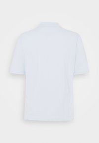 Polo bleu clair uni à manches courtes vu de dos sur fond blanc.