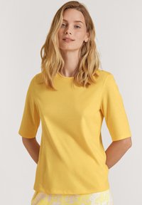 Geel t-shirt met korte mouwen, gemaakt van zachte stof. Heeft een ronde halslijn en een rechte zoom. Voelt glad aan met geen zichtbare patronen of accenten.