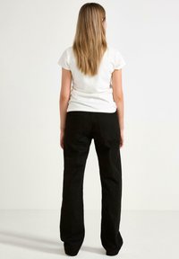 Pantaloni neri a gamba larga con una trama liscia, vita alta e tasche posteriori, abbinati a una t-shirt bianca a maniche corte.