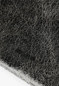 Superficie de cuero negro con una textura agrietada, que presenta un logo en relieve. El acabado es brillante con un sutil brillo.