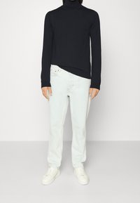 Czarny sweter z golfem i długimi rękawami, zestawiony z jasnoniebieskimi dżinsami o prostych nogawkach i białymi trampkami. Prosty, schludny design.