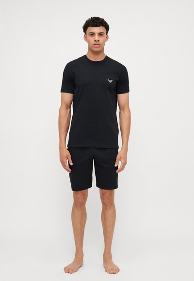 T-shirt nera a maniche corte con collo rotondo, caratterizzata da un piccolo logo sul petto, abbinata a pantaloni corti neri coordinati. Materiale in cotone, design semplice.