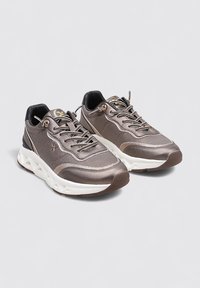 Zapatillas deportivas de malla marrón con suela de goma blanca. Presentan un diseño texturizado, punta redondeada, cierre de cordones en la parte frontal y detalle de logo en la lengüeta.