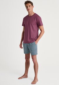 Heren t-shirt met korte mouwen in mauve, gecombineerd met zwembroeken met een patroon van roze en blauwe vierkanten. Zijzakken, casual fit en lichtgewicht stof.