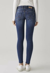 Tunna blå denimjeans med medelhög midja, bakfickor med sömdetaljer och en subtil blekt struktur. Bärs med vita sneakers.