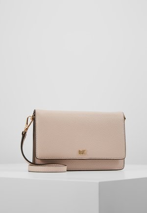 Pochette Michael Kors en cuir beige texturé avec logo MK doré et bracelet détachable, posée sur un socle blanc sur fond gris uni.