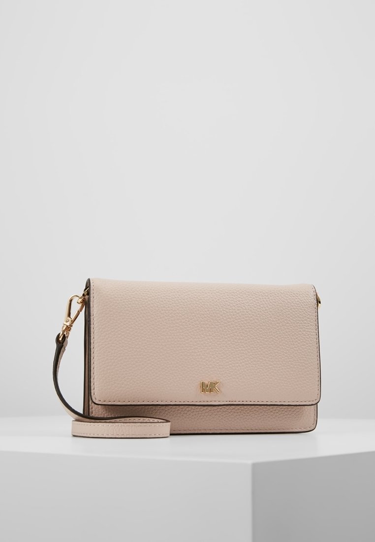 Pochette Michael Kors en cuir beige texturé avec logo MK doré et bracelet détachable, posée sur un socle blanc sur fond gris uni.