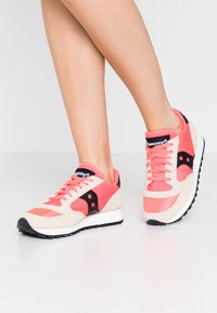 Rosa und schwarze Sport-Sneaker aus Wildleder und Mesh-Materialien, mit einer weißen Sohle, schwarzen Akzenten und einem auffälligen Logo auf der Zunge.