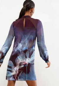 Gėlėmis margintas suknelė, pagaminta iš lengvos medžiagos. Suknelė turi ilgas puffy rankoves, aukštą apykaklę su rakto forma detalė ir tamsiai violetinės bei mėlynos spalvos gradientą.
