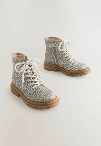 Botas tobilleras de estampado de leopardo marrón y gris con cordones, cremallera lateral y suela de goma texturizada. Forro interior suave para mayor comodidad.