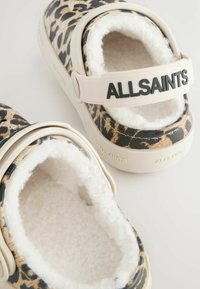 Musta ja beige leopardi-kuvioiset liukupohjaiset kengät, joissa on pehmeä valkoinen vuori, beigen värinen hihanauha, jossa lukee "ALLSAINTS", ja tekstuurilla varustetut kumipohjat.