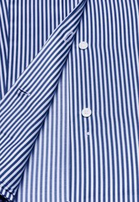 Camicia a righe con sottili strisce verticali blu navy e bianche, bottoni e materiale in cotone morbido con una texture liscia.