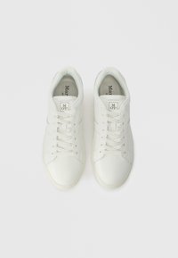 Ζευγάρι λευκών αθλητικών παπουτσιών με κορδόνια, βλέπεται από πάνω σε έναν απλό ανοιχτό γκρίζο φόντο.