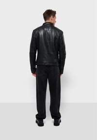 Chaqueta de cuero negra con un cuello alto, diseño ajustado, costuras en la espalda y mangas largas. Usada sobre pantalones negros y calzado.