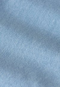 Lichtblauw denimstof met een zichtbare weefstructuur en subtiele schaduwen door plooien.