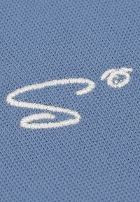 Helles blaues Textil mit einem weißen gestickten Design, das einem wirbelnden Buchstaben "S" mit einem kreisförmigen Akzent ähnelt. Sanfte Textur und glatte Oberfläche.