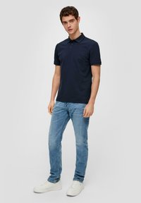 Granatowa koszulka polo z krótkimi rękawami, trzema guzikami, w slim fit, w połączeniu z jasnoniebieskimi dżinsami i białymi trampkami.