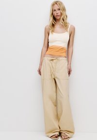 Lichtgewicht katoenen tanktop in crème en oranje met zonafbeelding, gecombineerd met losse, beige wijde broek met een trekkoord in de taille.