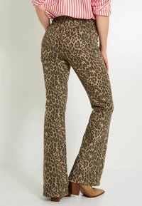 Pantalones de campana con estampado de leopardo en tonos marrones y negros, con una cintura alta y bolsillos traseros, combinados con zapatos de tacón cuadrado en color beige.