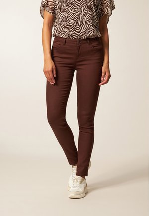 Bruine skinny jeans met een gladde textuur en voorzakken, gecombineerd met een geblokt shirt met korte mouwen en witte sneakers.