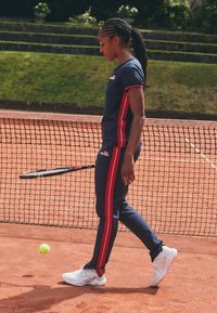 Conjunto de tenis que incluye una camiseta de manga corta en color azul marino con detalles en rojo y pantalones a juego con rayas laterales, combinados con zapatillas deportivas blancas.