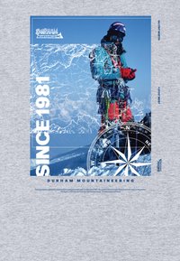 Horolezec v horolezeckém vybavení a helmě stojí na sněhu, překrytý mapou, kompasem a textem „Od roku 1981“ a „Durham Mountaineering.“