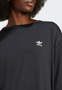 Top atletico nero realizzato in tessuto liscio, caratterizzato da una vestibilità ampia e un colletto largo. Il logo bianco di Adidas è posizionato sul petto.