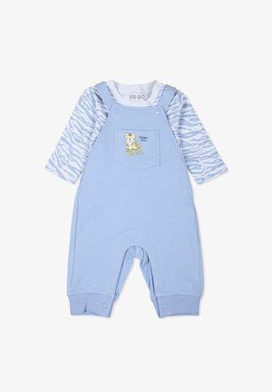 Salopette en coton bleu avec une poche arborant un motif de tigre jaune. Haut à manches longues en blanc avec des motifs abstraits bleus. Texture douce.