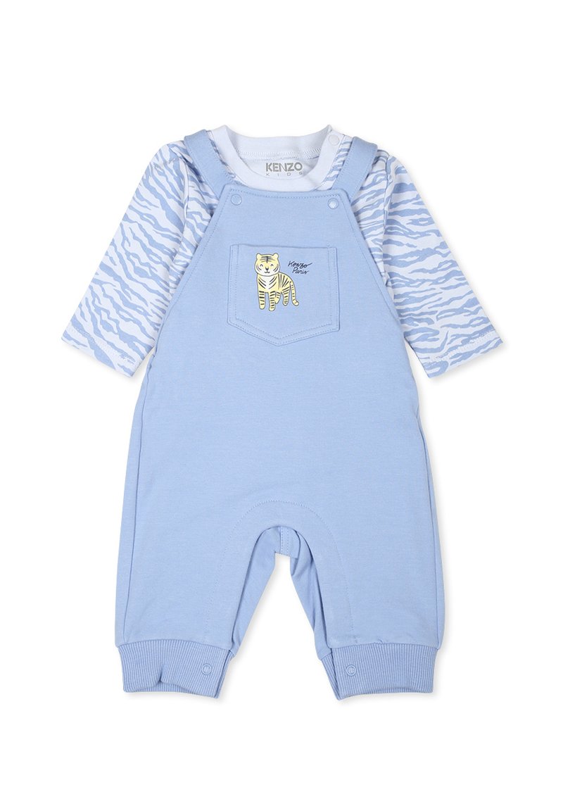 Salopette en coton bleu avec une poche arborant un motif de tigre jaune. Haut à manches longues en blanc avec des motifs abstraits bleus. Texture douce.