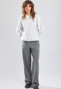 Gray sweatshirt with a casual design and a small purple logo. Paired with gray pinstriped pants and black platform boots.