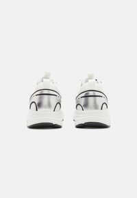 Hvite sneakers med en metallisk sølv hæl, med svarte detaljer og en teksturert såle, designet for komfort og stabilitet.