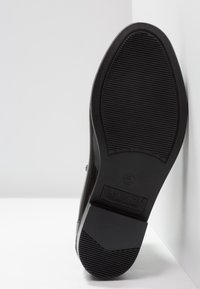 Semelle de chaussure noire avec grip texturé, arborant un bout arrondi. Marquée "LAUREN", présentant une finition lisse et un marquage discret.