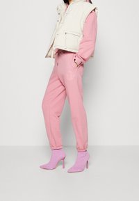 Pantalones de chándal rosa claro con un logo, combinados con un chaleco acolchado crema. El conjunto se completa con botas de tacón rosa con estampado.
