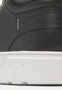 Svart lädersneaker med en vit gummisula. Funktioner inkluderar präglad logotyp och sömdetaljer som framhäver en elegant, minimalistisk design.