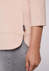 Tunic rosa chiaro con maniche a tre quarti, orlo curvo e spacco laterale, con un piccolo etichetta nera "socx". Materiale in cotone morbido.
