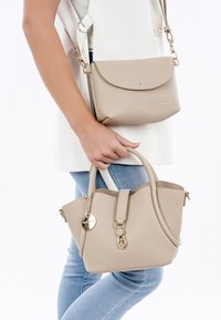 Beige leren handtassen set, bestaande uit een kleine crossbody met een klep en een middelgrote tote met een rits. Beide hebben gouden accenten en textuuroppervlakken.