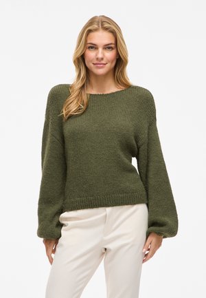 Pull en tricot vert à coupe décontractée, avec un ourlet côtelé et des manches ballons. Texture douce, encolure large et ronde, associé à un pantalon crème.