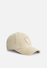 Casquette de baseball en velours côtelé beige avec une visière incurvée et un logo en relief à l'avant, dotée de détails cousus et de trous de ventilation.