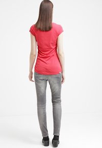 Camiseta ajustada de algodón roja con mangas cortas, combinada con jeans ajustados grises claros y botas de plataforma negras, vista desde la parte posterior.