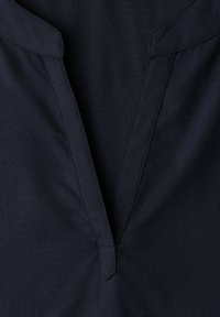 Vêtement bleu marine foncé avec un col en V et des coutures apparentes le long du col et des bords.