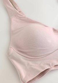 Šviesiai rožinė minkšta medvilninė liemenėlė su formuotais puodeliais, reguliuojamomis petnešėlėmis ir be siūlių kraštais, pasižyminti lygiu tekstūru ir minimalizuotu dizainu.