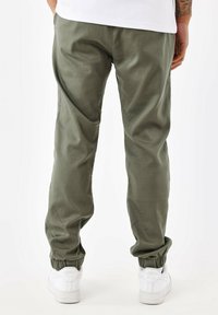 Pantalones jogger de color verde oliva con puños elásticos, textura suave y un ajuste relajado, combinados con zapatillas blancas.
