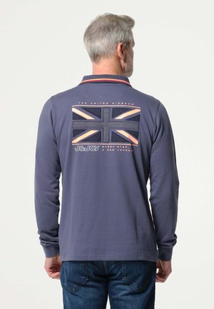 Polo à manches longues bleu marine avec un col rayé rouge et blanc. Présente un emblème texturé du drapeau britannique et le texte "LE ROYAUME-UNI".