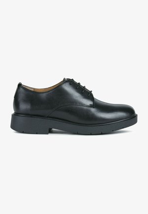 Zapatos de cuero negro con cordones, con un acabado suave, punta redonda y una suela de goma negra gruesa. Presenta detalles de costura sutiles.