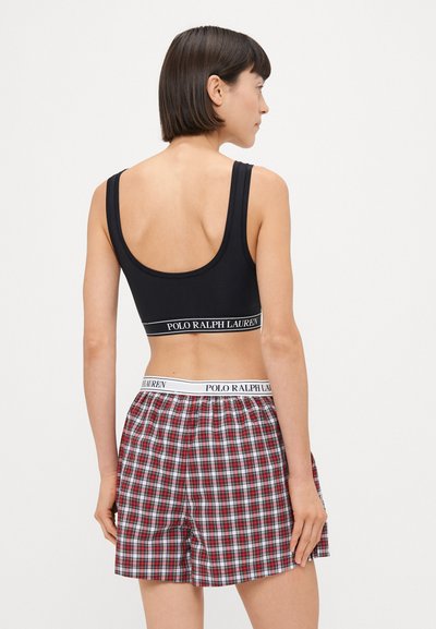Μαύρο κοντό αμάνικο τοπ με λογότυπο, συνδυασμένο με χαλαρές κόκκινες και λευκές καρό σορτς με ελαστική μέση.